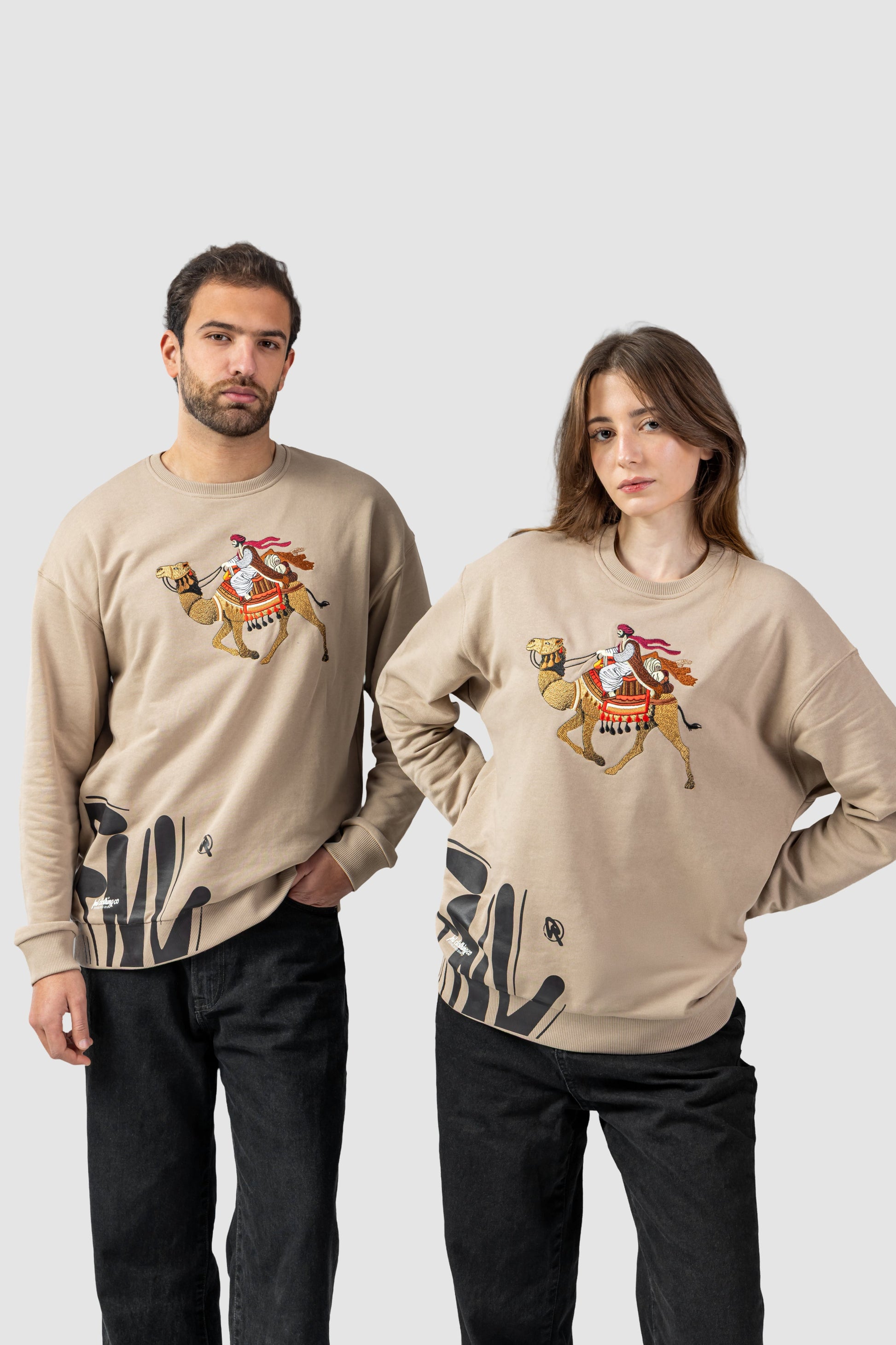 Two people wearing beige sweaters with graphic designs on a white background